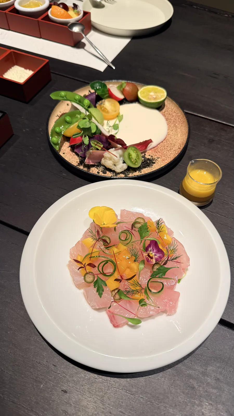 薄切りの魚に花や野菜を添えた白い皿と、野菜の皿が並ぶ客室での夕食