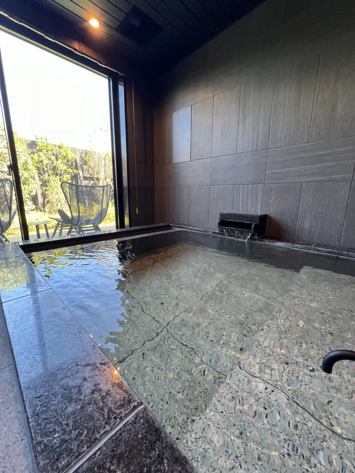 窓から緑が見える開放的な客室露天風呂。湯が張られている様子。