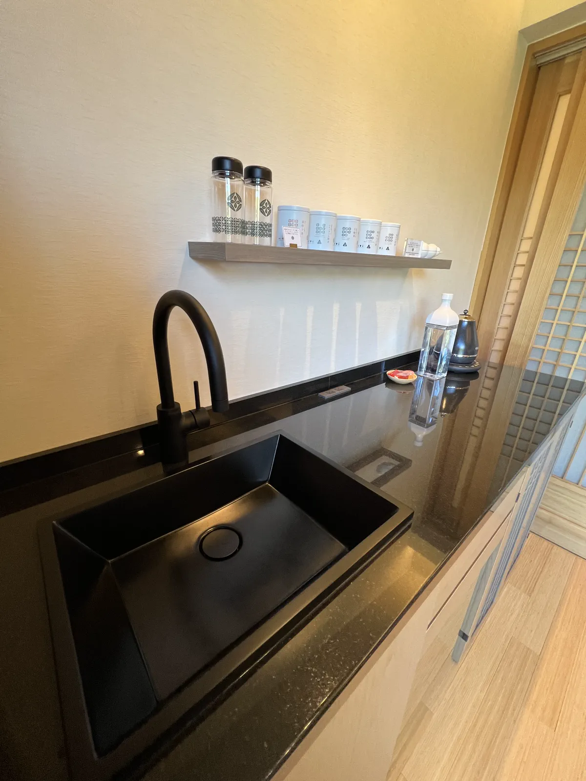 旅館の客室ミニバーにある黒いシンクと棚。おしゃれなボトルやカップが並ぶ。