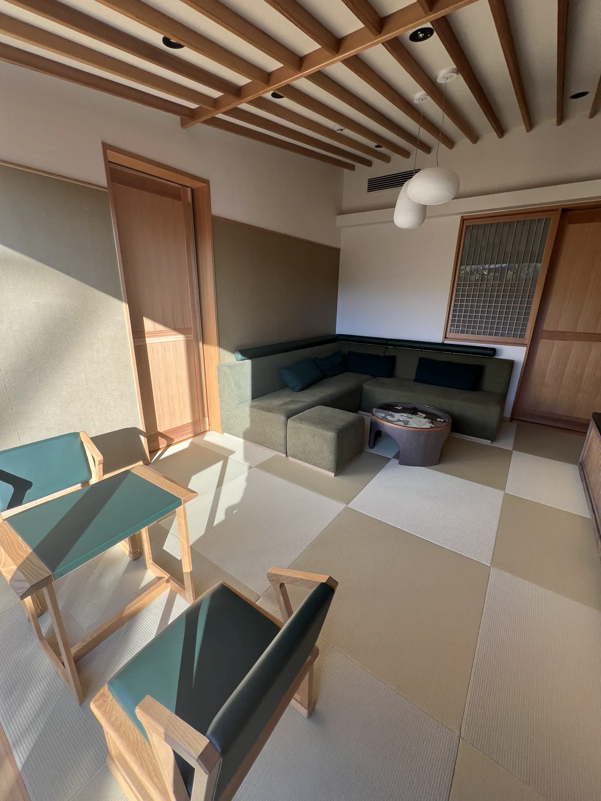 畳敷きの広々とした和モダンな客室リビング。木格子天井と緑のソファが落ち着いた空間を演出。