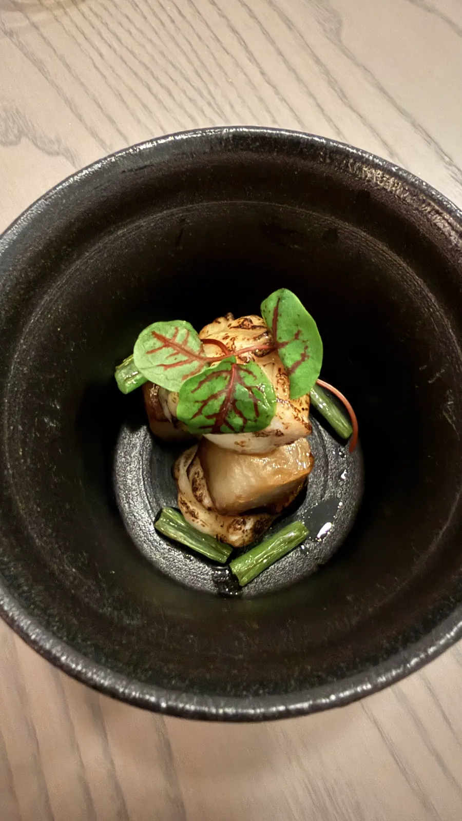 焼き目をつけた厚切りふぐと青菜を黒い器に盛り付けたグリリア